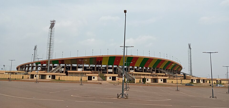 Vue extérieure du stade : la façade circulaire est peinte aux couleurs du drapeau camerounais, vert, rouge et jaune.